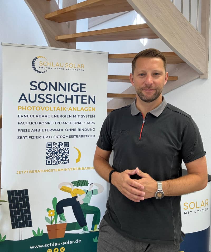 Inhaber der Photovoltaik-Installationsfirma und Solarberatung Schlau Solar GmbH Dirk Schlünz steht vor einem Werbebanner in einem Haus.
